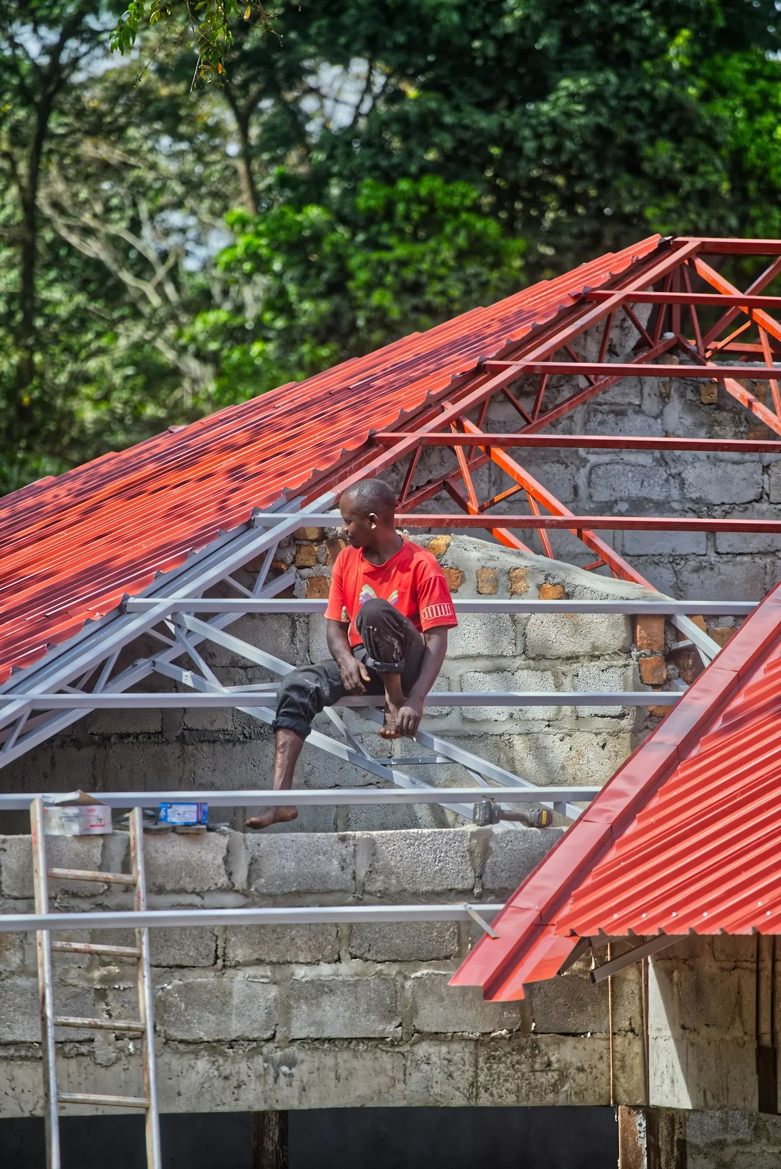 Pekerja memasang genteng metal merah baru pada rangka atap di Rawalumbu